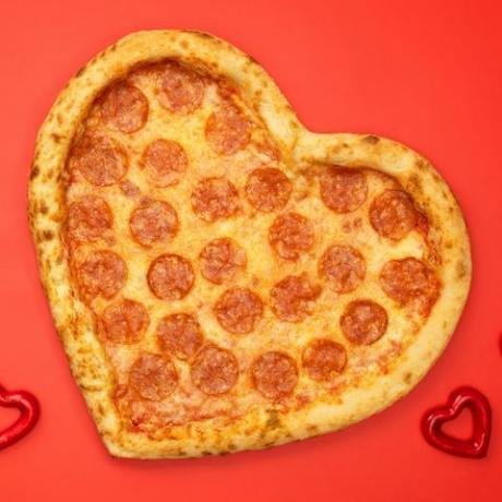 Pepperoni pizza în formă de inimă pentru ziua Îndrăgostiților pe fundal de hârtie roșie