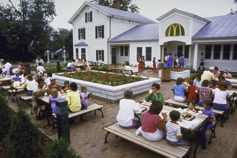 Restaurantul McDonald este văzut din exterior în cazul în care oamenii mănâncă în aer liber la mese de picnic. Exteriorul clădirii are un aspect clasic han țară unusal