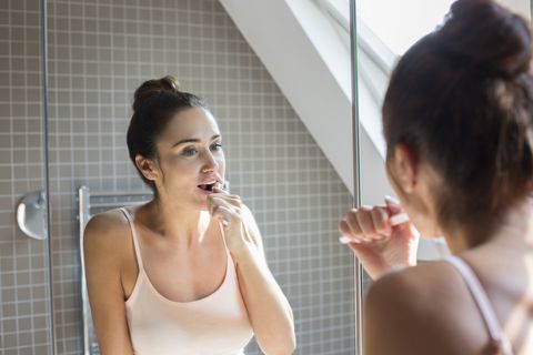 Mid adult femeie spalatul pe dinti in oglinda de la baie.