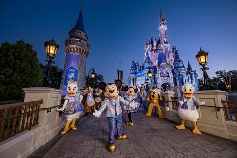 mouse-ul mickey și prietenii purtând haine strălucitoare pentru cea de-a 50-a aniversare în timp ce pozează în fața castelului Cenușăreasa din parcul Regatul Magic