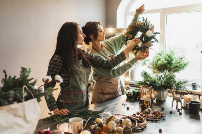 două femei care fac coroană de Crăciun folosind ramuri proaspete de pin și decorațiuni festive